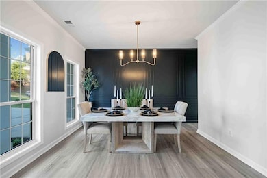 Dining area featuring a chandelier, baseboards, light wood finished floors, crown molding, and a decorative wall