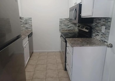 Kitchen featuring appliances with stainless steel finishes, white cabinetry, backsplash, and light tile patterned flooring