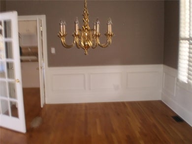 Unfurnished dining area with wainscoting, a chandelier, wood finished floors, and a decorative wall