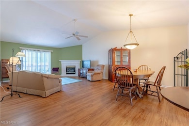 Dining area featuring wood finished floors, vaulted ceiling, a ceiling fan, and a glass covered fireplace