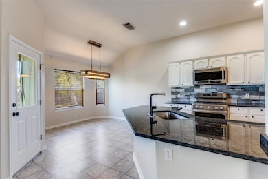 Kitchen featuring dark stone counters, white cabinets, stainless steel appliances, tasteful backsplash, and vaulted ceiling
