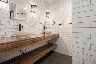 Fully Renovated Bath with Walls of Classic White Subway Tile, Dual Bowl Sinks, a Custom Wood Vanity, and a Spacious Shower with a Built-In Bench.