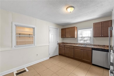 Kitchen featuring dark countertops, stainless steel appliances, light tile patterned flooring, a textured ceiling, and dark brown cabinets