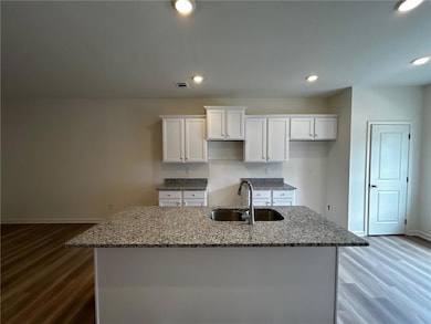 Kitchen featuring white cabinets, a center island with sink, stone countertops, wood finished floors, and recessed lighting