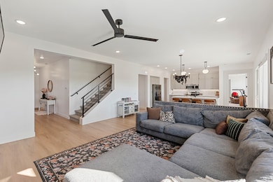 Living room featuring stairs, recessed lighting, light wood-type flooring, a ceiling fan, and a chandelier
