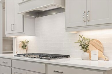 Kitchen featuring custom exhaust hood, stainless steel gas stovetop, light countertops, and backsplash