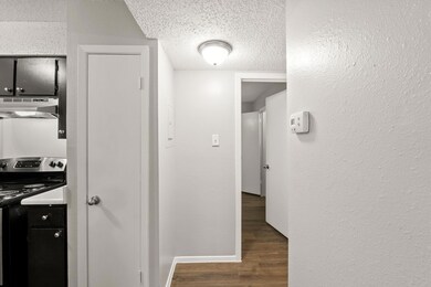 Hallway featuring dark wood-type flooring, a textured ceiling, and a textured wall