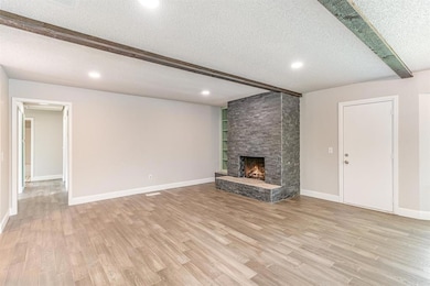 Unfurnished living room with a textured ceiling, light wood-type flooring, a fireplace, beamed ceiling, and recessed lighting