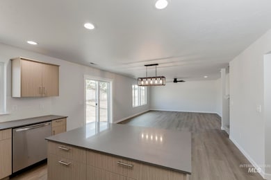 Kitchen featuring light brown cabinetry, hanging light fixtures, dishwasher, a ceiling fan, and light wood finished floors