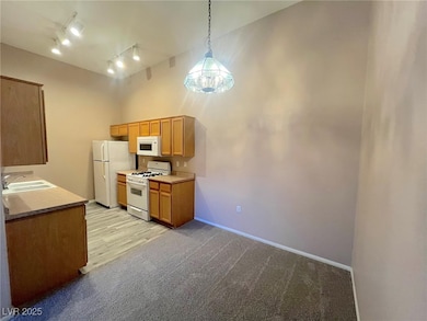 Kitchen with white appliances, light carpet, light countertops, rail lighting, and hanging light fixtures