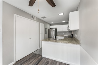 Kitchen with electric stove, freestanding refrigerator, dark wood-style flooring, white cabinetry, and a peninsula