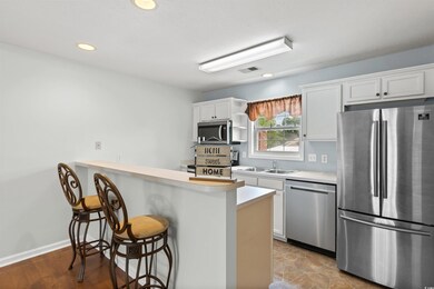 Kitchen featuring stainless steel appliances, a kitchen bar, light countertops, white cabinetry, and recessed lighting