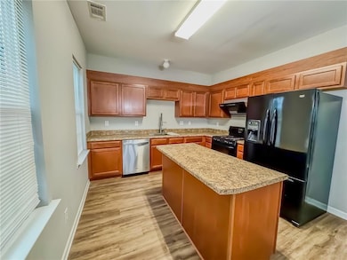 Kitchen with black appliances, light wood-style flooring, a kitchen island, and extractor fan