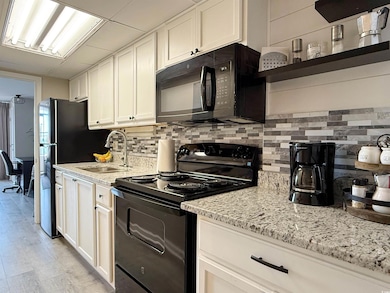Kitchen with black appliances, a sink, tasteful backsplash, and light stone counters