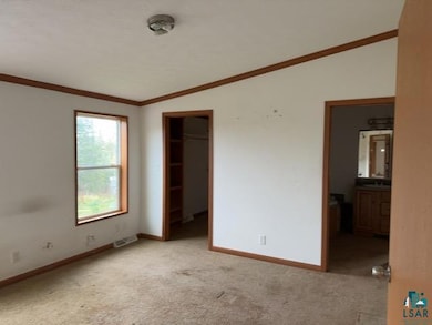 Unfurnished bedroom with vaulted ceiling, light carpet, baseboards, crown molding, and ensuite bath