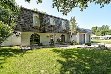View of front of property featuring mansard roof, brick siding, an attached garage, driveway, and a front yard