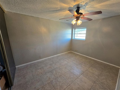 Empty room with a textured wall, a textured ceiling, light tile patterned floors, and a ceiling fan