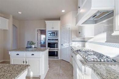 Kitchen with backsplash, white cabinetry, light ti