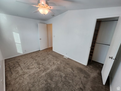 Unfurnished bedroom featuring carpet flooring, vaulted ceiling, and ceiling fan