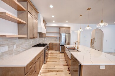 Kitchen featuring appliances with stainless steel finishes, beverage cooler, custom range hood, pendant lighting, and light stone counters