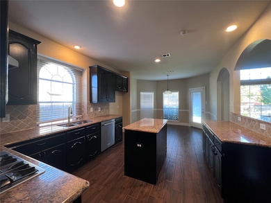 Kitchen featuring decorative backsplash, a kitchen island, dark cabinets, dark wood-style flooring, and pendant lighting