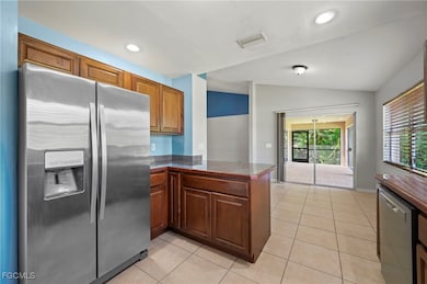 Kitchen with stainless steel appliances, vaulted ceiling, light tile patterned floors, tile counters, and brown cabinets