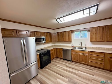 Kitchen with appliances with stainless steel finishes, crown molding, light wood finished floors, a textured ceiling, and brown cabinetry