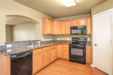 Kitchen with black appliances, a textured ceiling, light wood-style floors, dark stone counters, and arched walkways