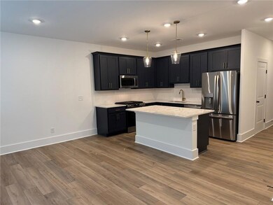Kitchen featuring appliances with stainless steel finishes, a sink, baseboards, wood finished floors, and recessed lighting