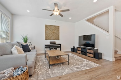 Living room with stairs, ceiling fan, wood finished floors, and recessed lighting