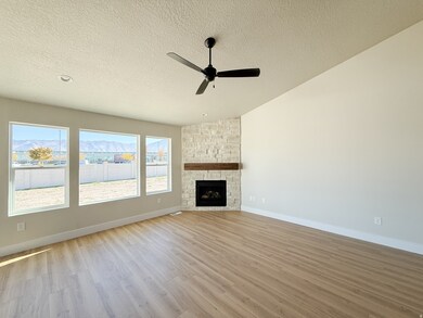 Unfurnished living room with vaulted ceiling, light wood finished floors, a fireplace, a textured ceiling, and a ceiling fan