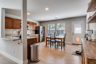 Kitchen with brown cabinetry, dark stone counters, recessed lighting, light wood-style floors, and stainless steel appliances