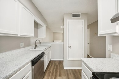 Kitchen with dark wood-style floors, stainless steel dishwasher, white cabinetry, black range oven, and light stone counters