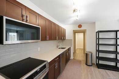 Kitchen featuring appliances with stainless steel finishes, light wood-type flooring, tasteful backsplash, light countertops, and dark brown cabinetry