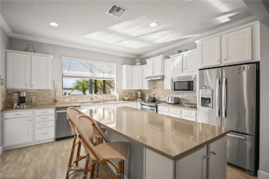Kitchen with stainless steel appliances, under cabinet range hood, a center island, crown molding, and white cabinetry
