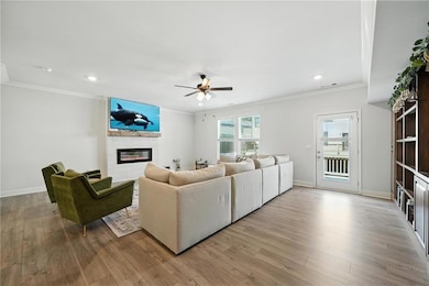 Living room with ornamental molding, a fireplace, a ceiling fan, wood finished floors, and recessed lighting