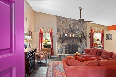 Living area featuring lofted ceiling, dark wood-style flooring, a stone fireplace, a ceiling fan, and a textured ceiling