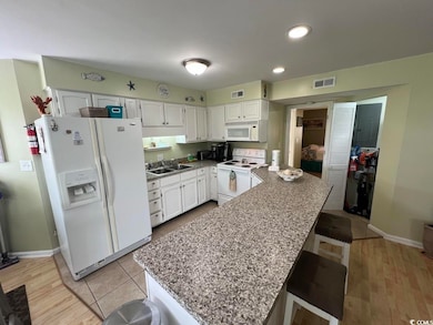 Kitchen featuring white appliances, white cabinets, a peninsula, a kitchen bar, and recessed lighting
