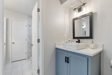 Full bath with vanity, a shower stall, light tile patterned floors, and a textured wall