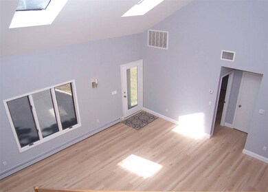 Spare room featuring a skylight, high vaulted ceiling, a baseboard radiator, and wood finished floors
