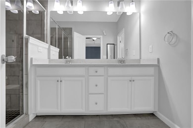 Full bath with double vanity, a shower stall, tile patterned flooring, and baseboards
