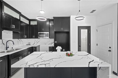 Kitchen with dark cabinetry, stainless steel microwave, light stone counters, and a sink