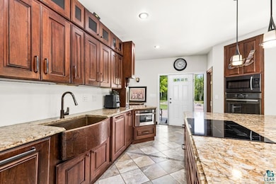 Kitchen featuring black appliances, a sink, light tile patterned floors, light stone countertops, and recessed lighting