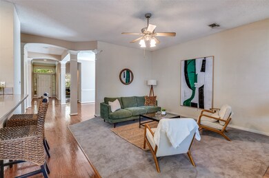 Living area featuring ornate columns, wood finished floors, arched walkways, a ceiling fan, and a textured ceiling