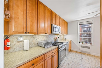 Kitchen featuring radiator, appliances with stainless steel finishes, a sink, baseboards, and tasteful backsplash