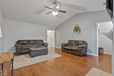Spacious living area with vaulted ceilings, rich wood flooring, and a cozy fireplace as the focal point. Large windows allow natural light to fill the space, creating a warm and inviting atmosphere.