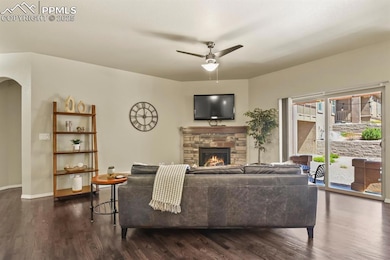 Living area with arched walkways, a fireplace, dark wood-type flooring, and ceiling fan