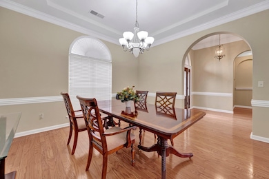 Dining area with a chandelier, arched walkways, a raised ceiling, light wood-type flooring, and baseboards