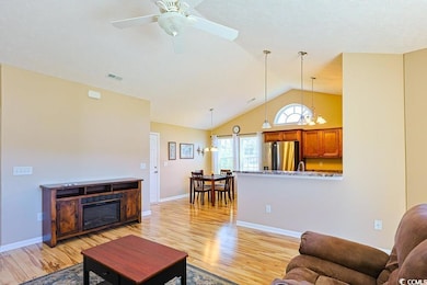 Living room with a chandelier, light wood-style floors, a glass covered fireplace, high vaulted ceiling, and a ceiling fan