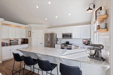 Kitchen with backsplash, white cabinetry, stainless steel appliances, crown molding, and light stone countertops